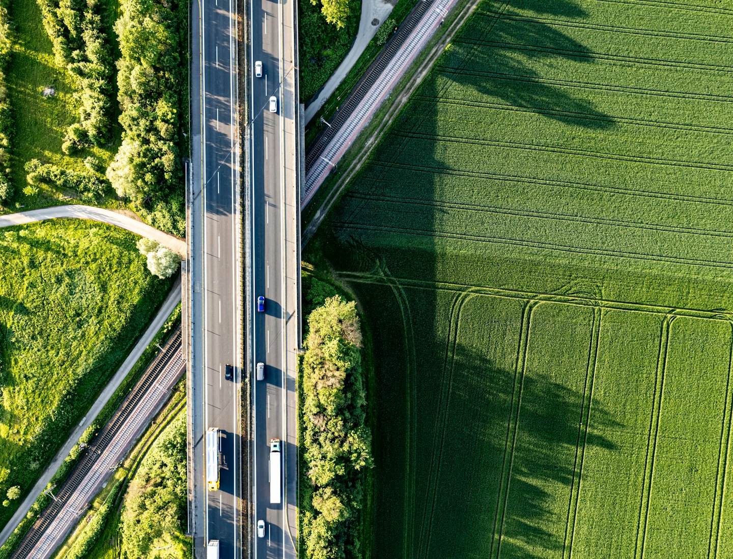 Autostrada e binari del treno attraversano campi verdi.