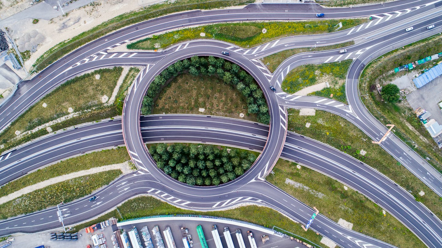 Vista aerea di un trafficato svincolo autostradale con una rotatoria centrale.
