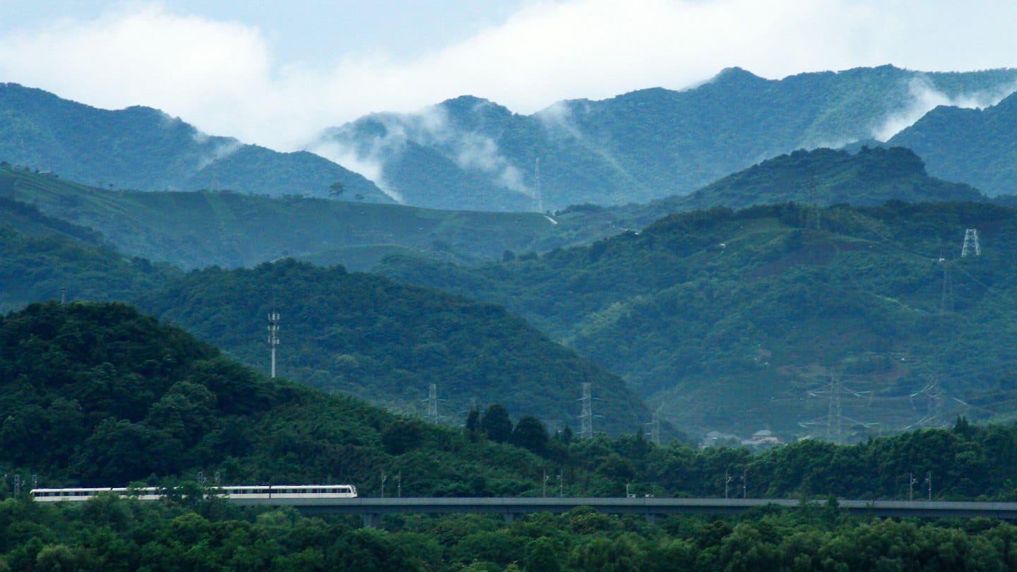 Un treno ad alta velocità viaggia su binari sopraelevati tra montagne verdi.