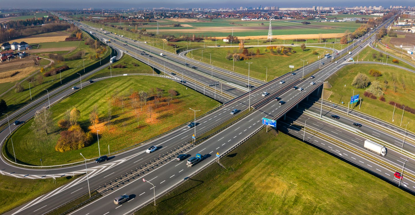 Automobili percorrono un svincolo autostradale a più livelli vicino a campi verdi.